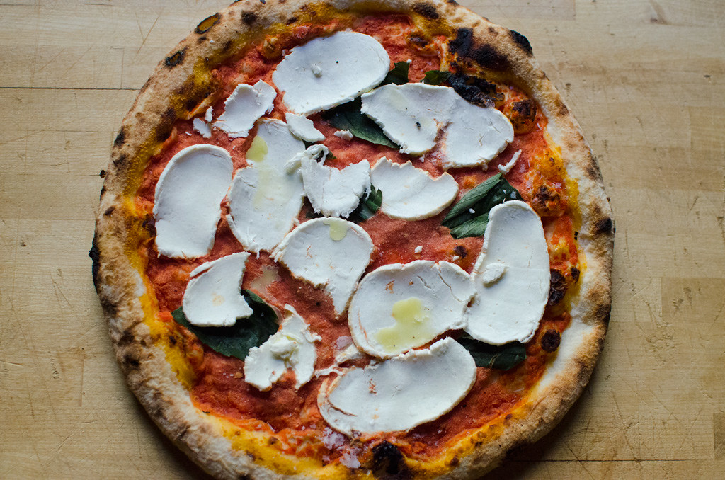 Freshly baked Burrata Pizza on a rustic table, garnished with basil and cherry tomatoes, illustrating the perfect blend of creamy cheese and crispy crust