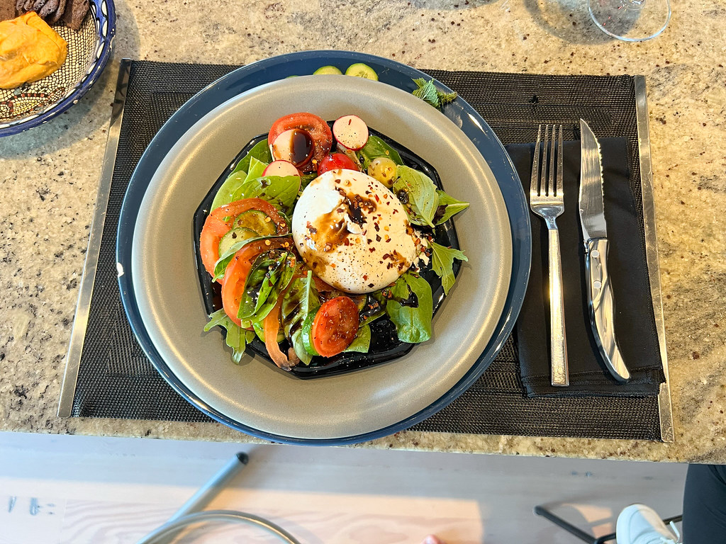 Bowl of fresh burrata salad with lush greens, ripe cherry tomatoes, sliced avocado, and a creamy burrata on top, drizzled with balsamic dressing