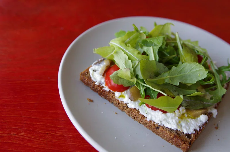 A plate of gourmet burrata toast topped with fresh basil and ripe cherry tomatoes, served on a rustic wooden table