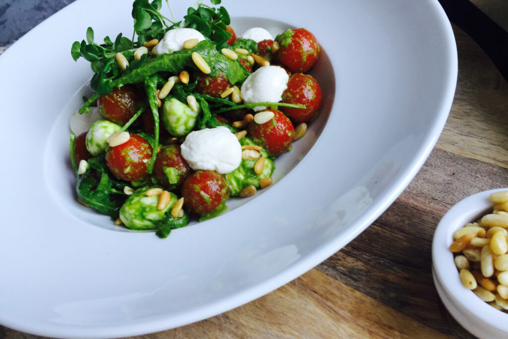 Colorful burrata salad topped with fresh greens, vibrant citrus, and drizzled with a light dressing on a white ceramic plate