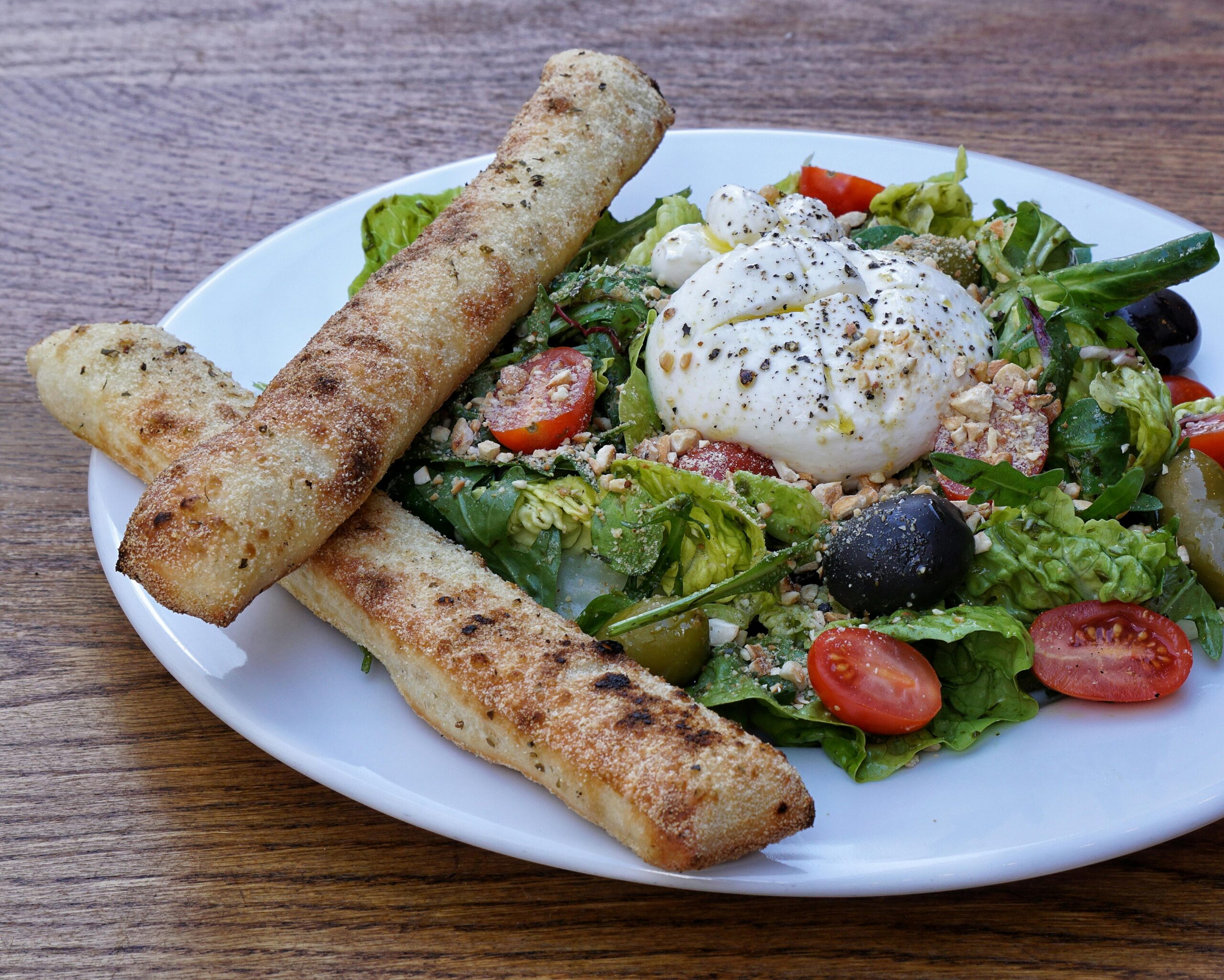 Gourmet pizza with burrata cheese, grilled vegetables, and fresh basil on a rustic wooden t