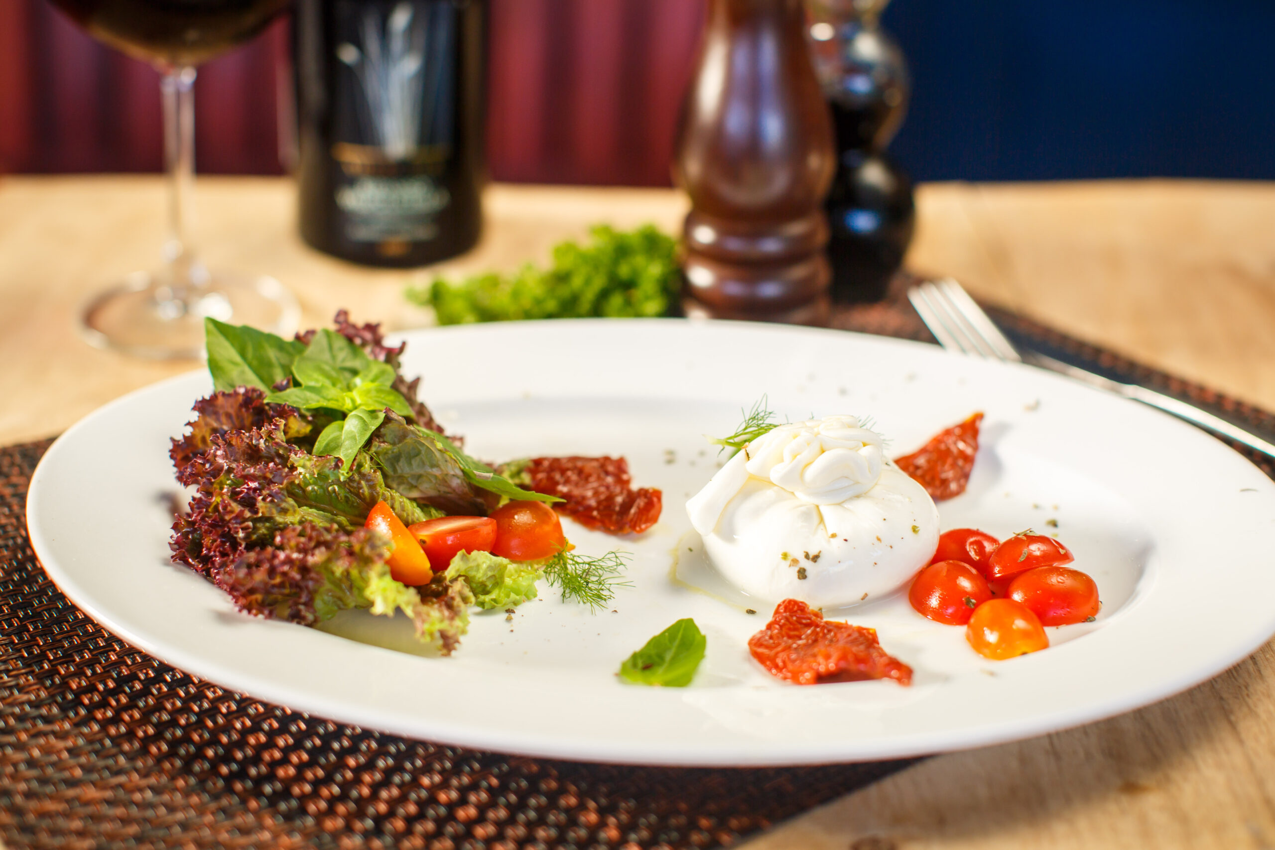 Elegant burrata appetizer with heirloom tomatoes and fresh basil on a rustic wooden board.